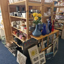 Houten tafel met blauwe vazen, gele bloemen en diverse huishoudartikelen, kasten met servies en decoratieve spullen op achter