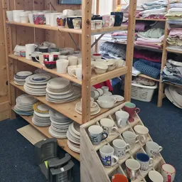 Houten stellingen met gestapeld serviesgoed, kopjes en borden, met textiel op achtergrond