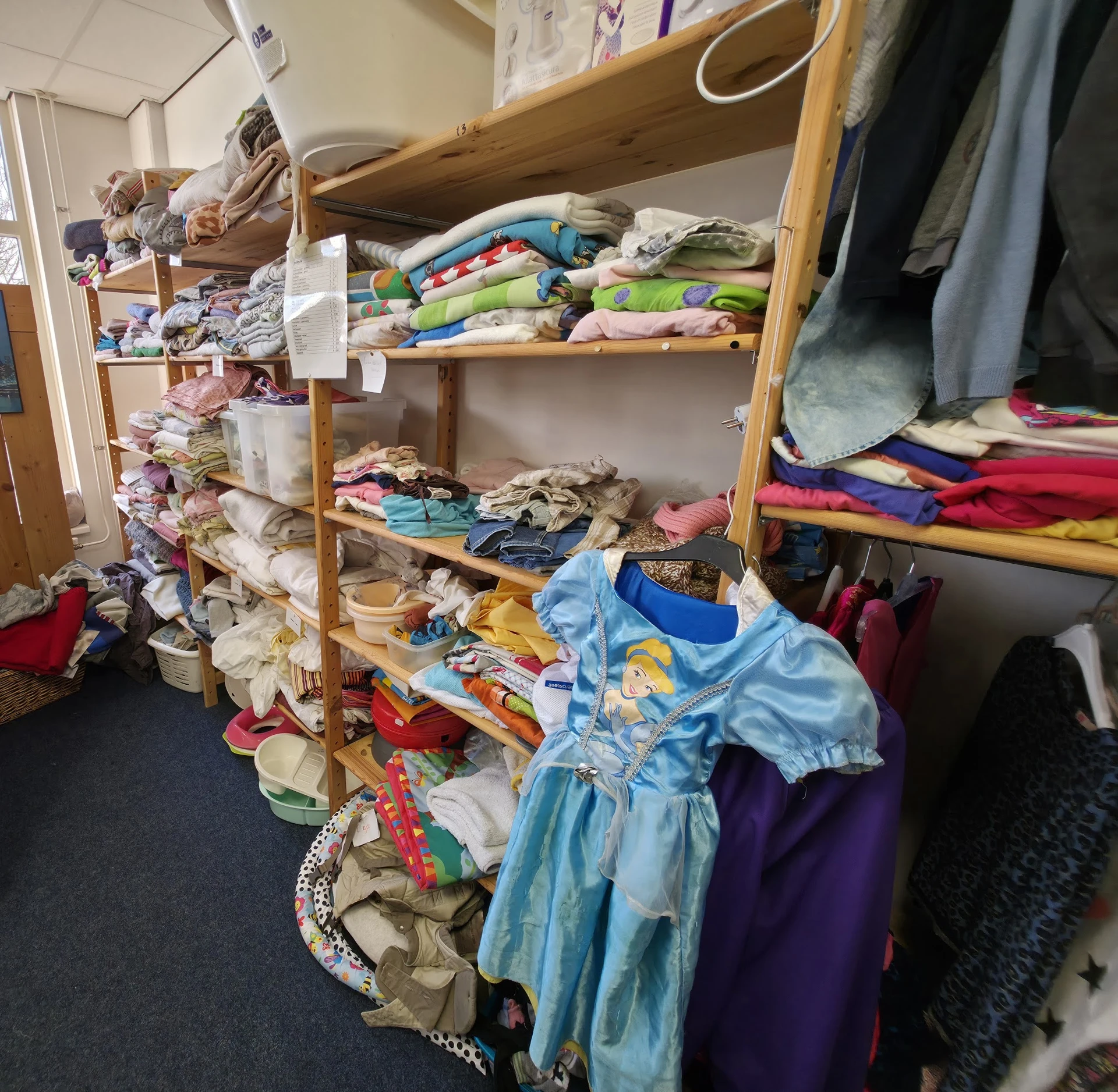 Houten stellingen met kleding, waaronder jurken, truien en andere textiel netjes uitgestald
