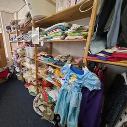 Houten stellingen met kleding, waaronder jurken, truien en andere textiel netjes uitgestald