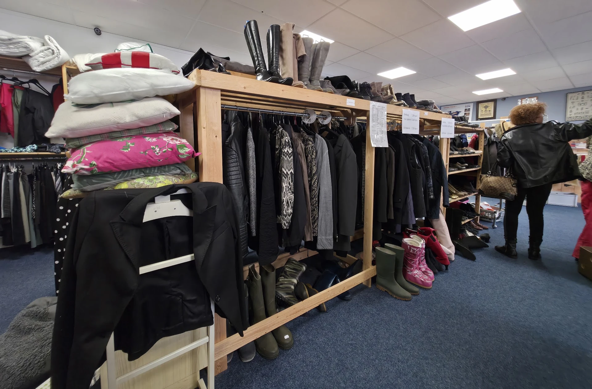 Houten stellingen met tweedehands kleding, schoenen en accessoires in een kringloopwinkel