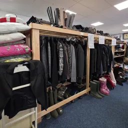 Houten stellingen met tweedehands kleding, schoenen en accessoires in een kringloopwinkel