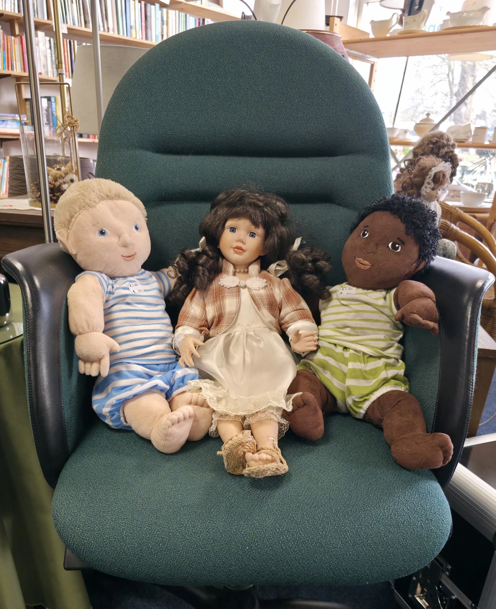Drie stoffige poppen in kinderjurken zittend op een groene fauteuil
