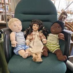 Drie stoffige poppen in kinderjurken zittend op een groene fauteuil