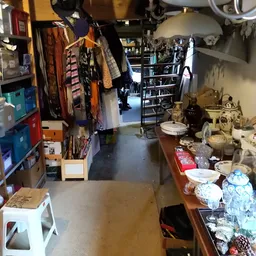 Binnenaanzicht van kringloopwinkel met kledingrekken links, kasten met spullen rechts en tafel met servies voorgrond