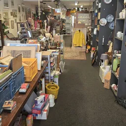 Winkelvloer met verschillende stellingen, dozen, huishoudelijke artikelen en kleding in een kringloopwinkel