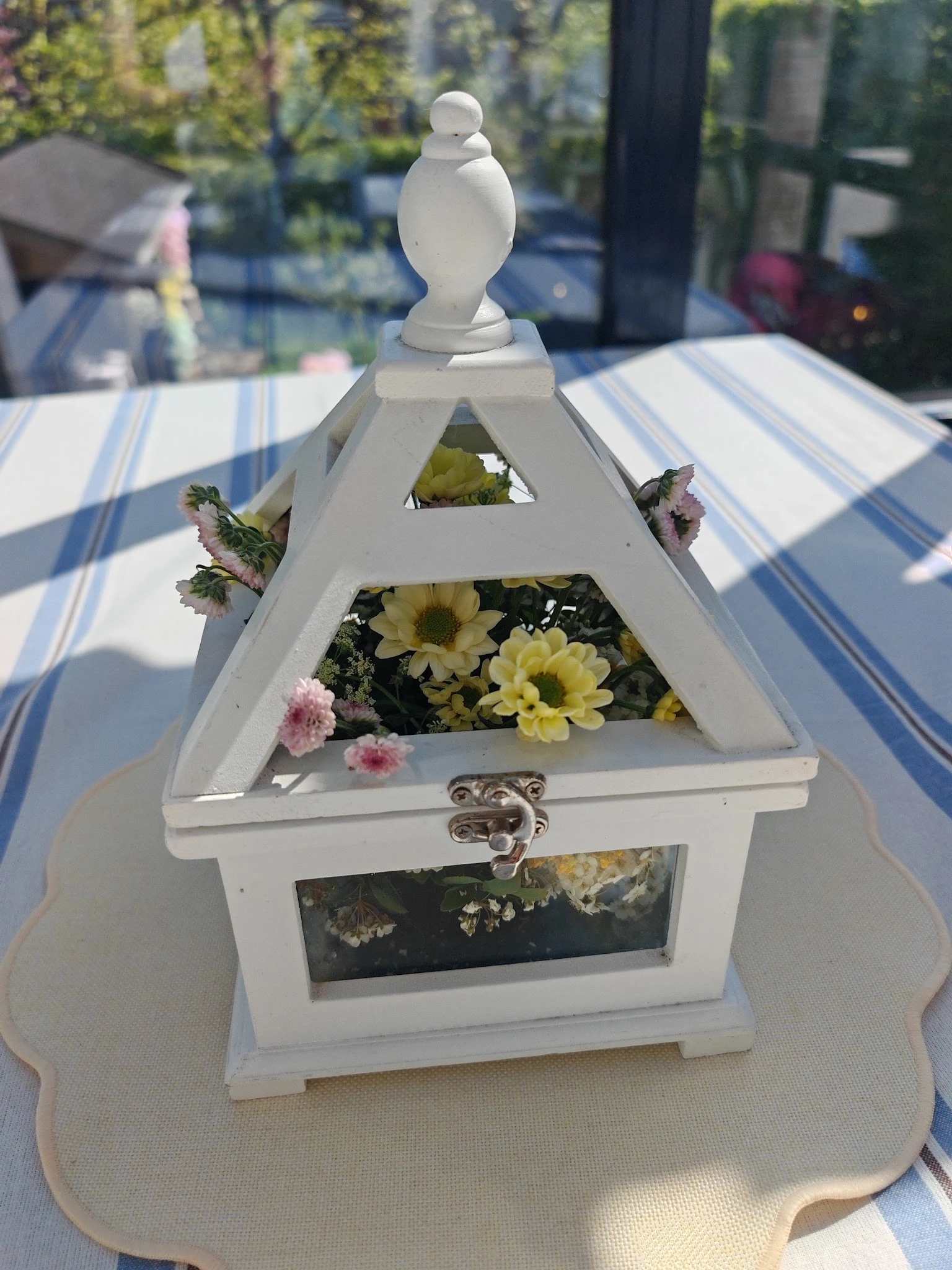 Witte houten vogelhuisje met gele en roze bloemen op een gestreept tafelkleed