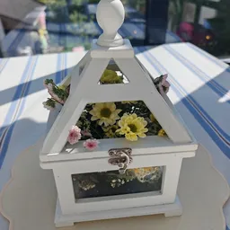 Witte houten vogelhuisje met gele en roze bloemen op een gestreept tafelkleed