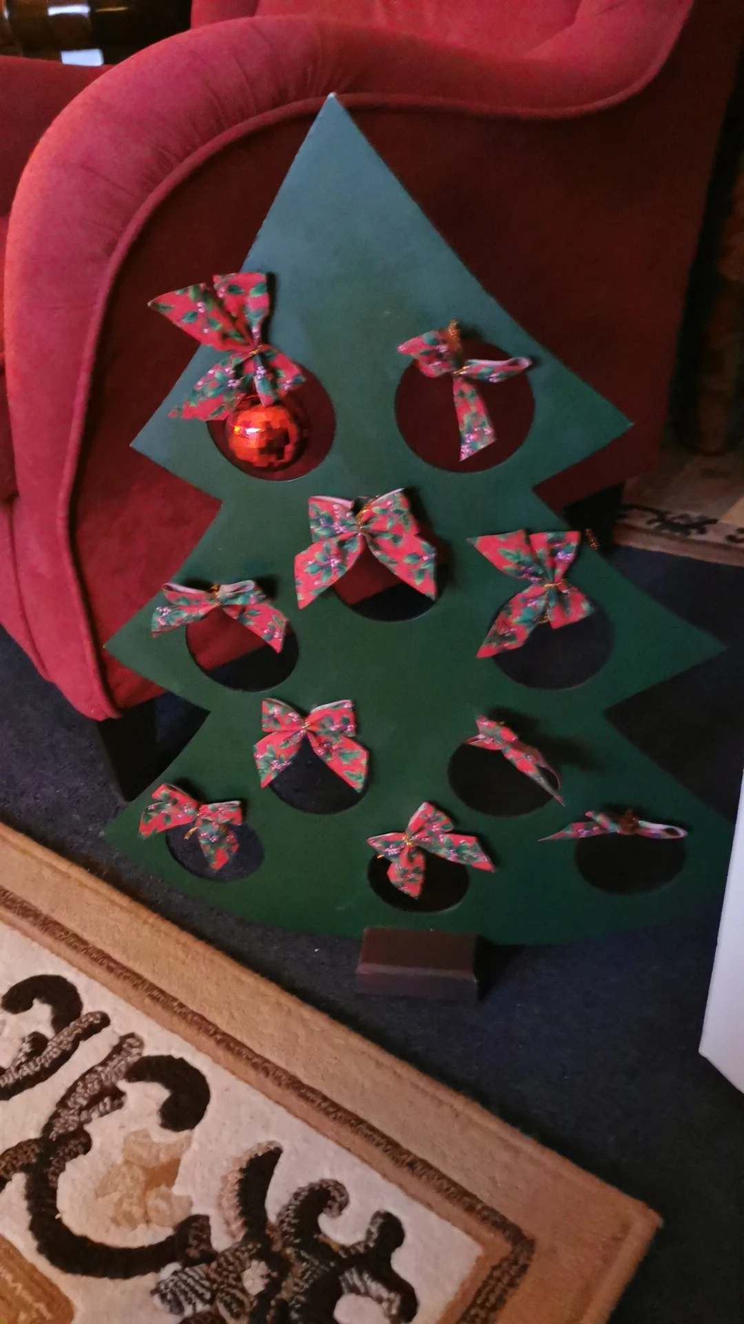 Groene kerstboom van karton versierd met rode kerstballen en rode strikjes als decoratie