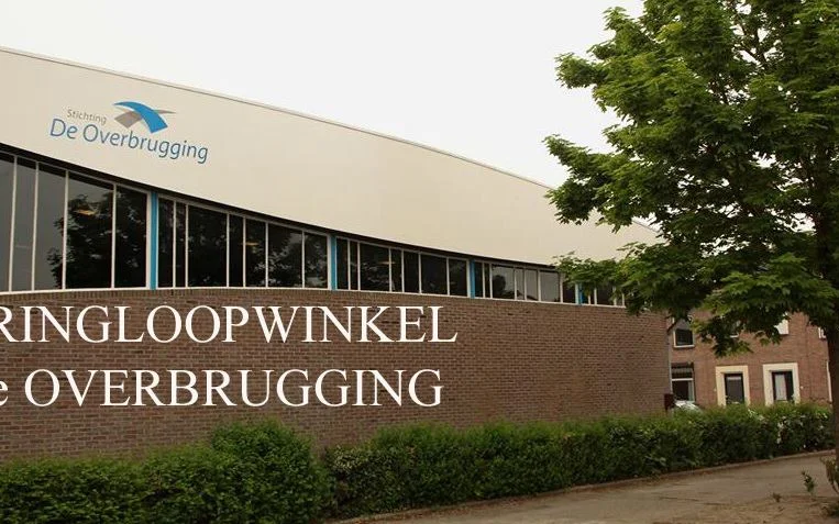 Gevel van kringloopwinkel met bakstenen muur en grote ramen, winkelnaam duidelijk zichtbaar