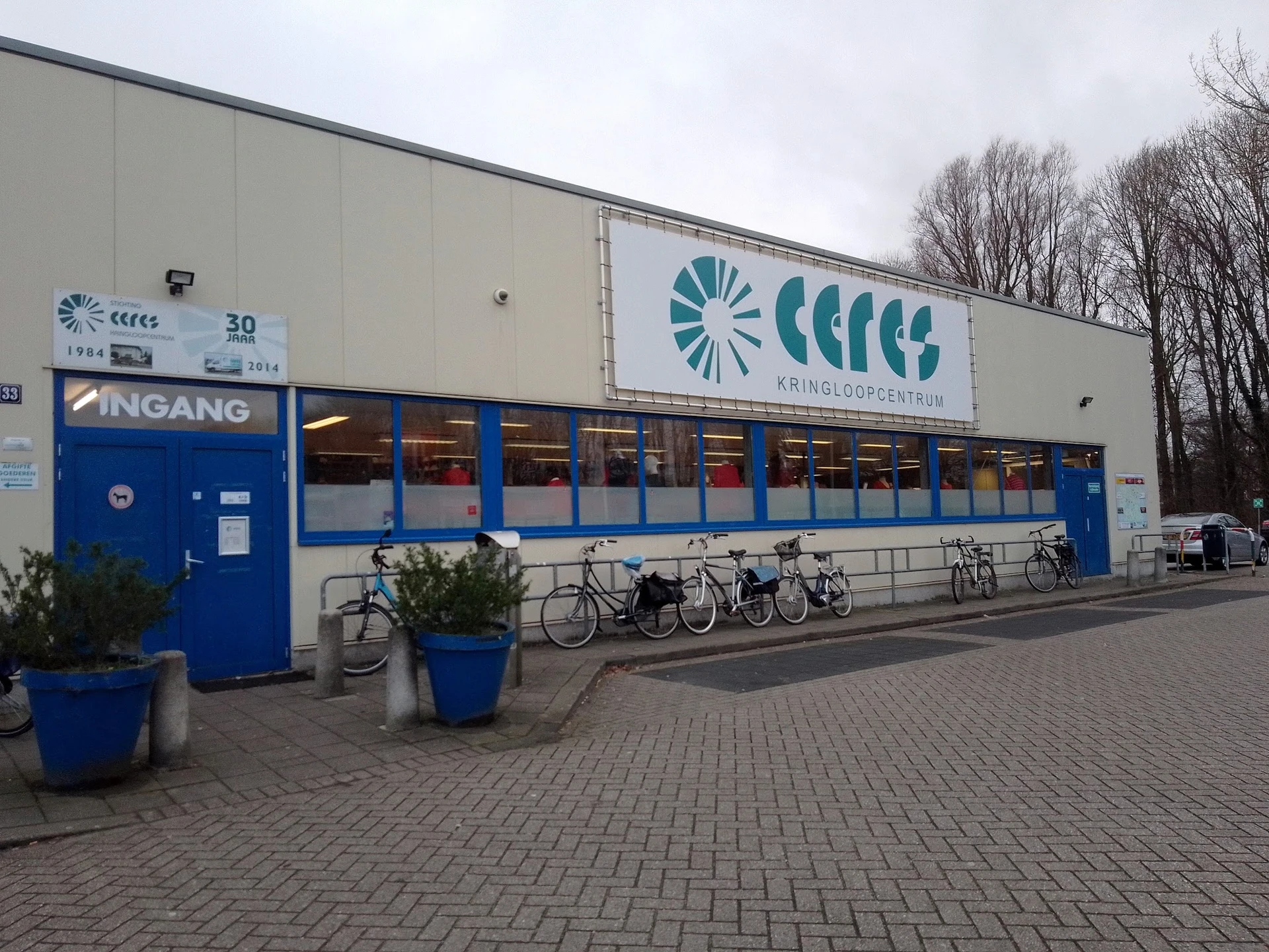 Voorgevel van kringloopwinkel Ceres met blauwe ingang, logo en fietsenrek