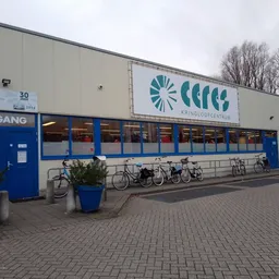 Voorgevel van kringloopwinkel Ceres met blauwe ingang, logo en fietsenrek
