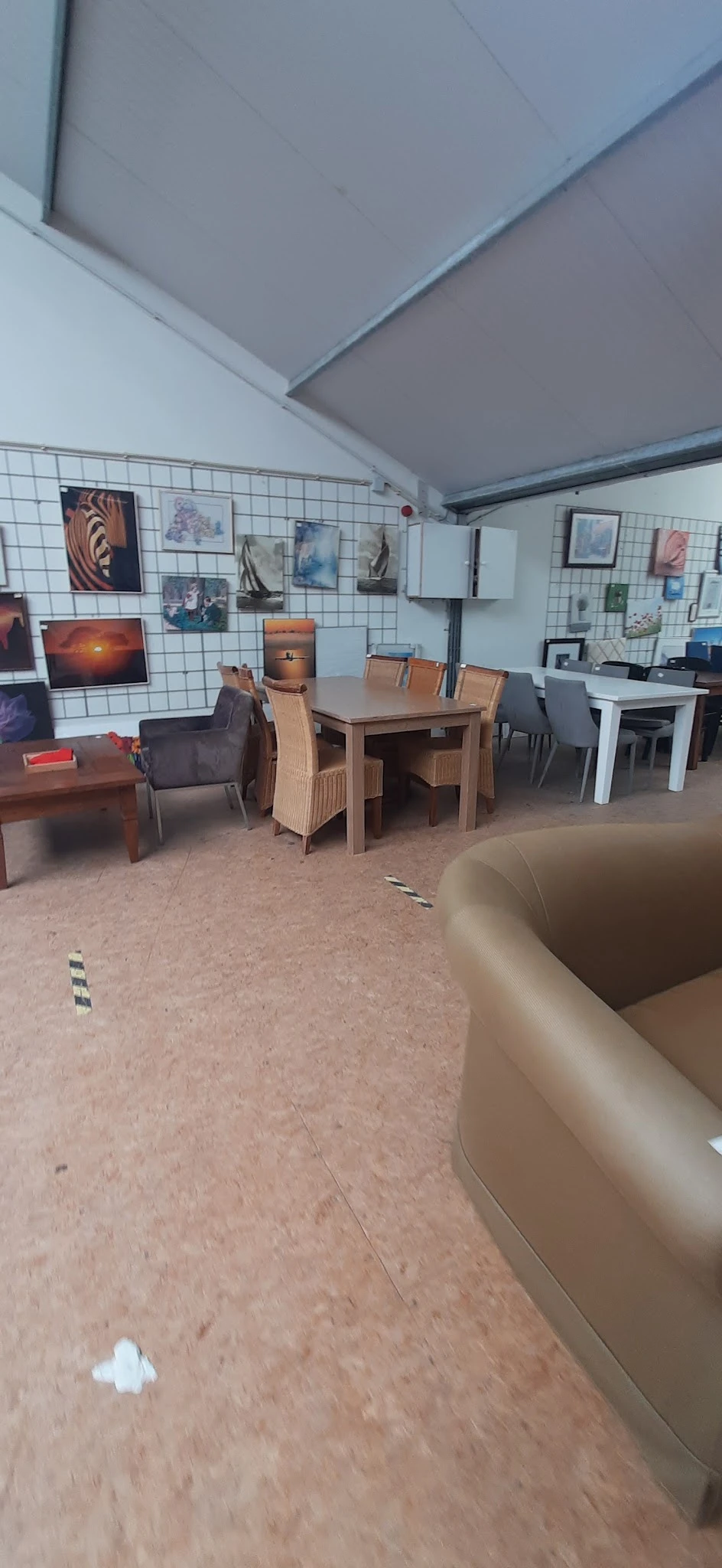 Winkelvloer met houten eettafel, stoelen en diverse meubels tegen witmgetegelde wand met opgegangen kunstwerken