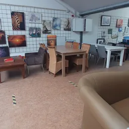 Winkelvloer met houten eettafel, stoelen en diverse meubels tegen witmgetegelde wand met opgegangen kunstwerken