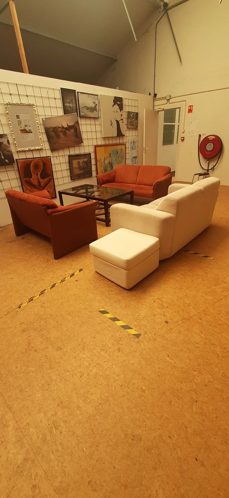 Tweedehands zitmeubels in diverse kleuren opgesteld in de winkel, met oranje stoelen en een crèmekleurige fauteuil met voeten