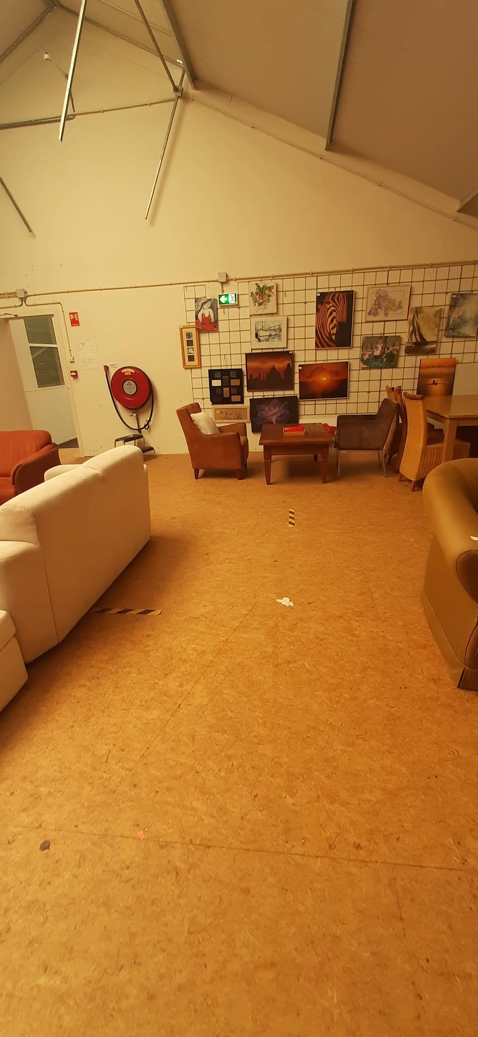 Zithoek in kringloopwinkel met fauteuils, bank en tafels op kurkvloer, kunstwerken aan wand