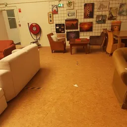 Zithoek in kringloopwinkel met fauteuils, bank en tafels op kurkvloer, kunstwerken aan wand