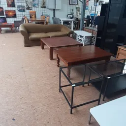 Verschillende houten tafels en een beige bank uitgestald op de winkelvloer