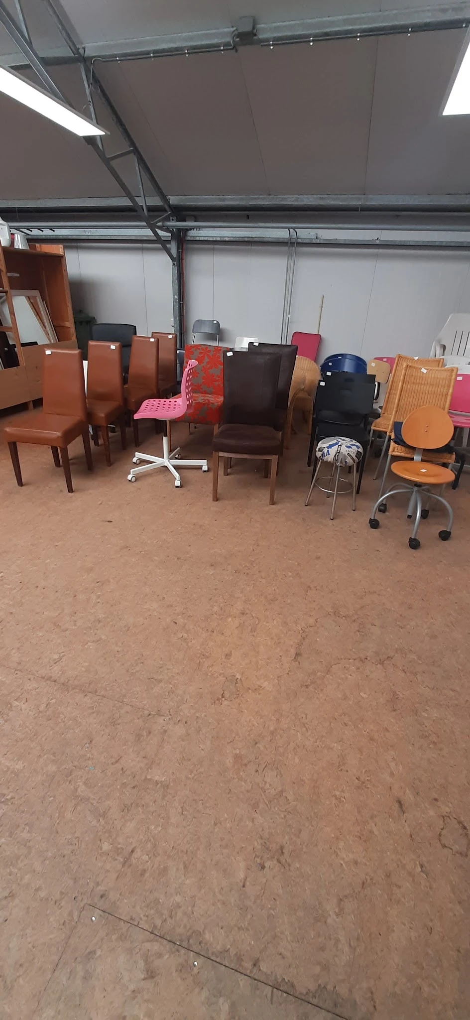 Diverse stoelen en zitmeubelen op de winkelvloer, waaronder bruine stoelen, een roze stoel en baarkrukken