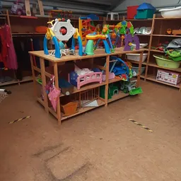 Houten speelhuisje met gekleurde speelgoed en accessoires op kringloopwinkel vloer