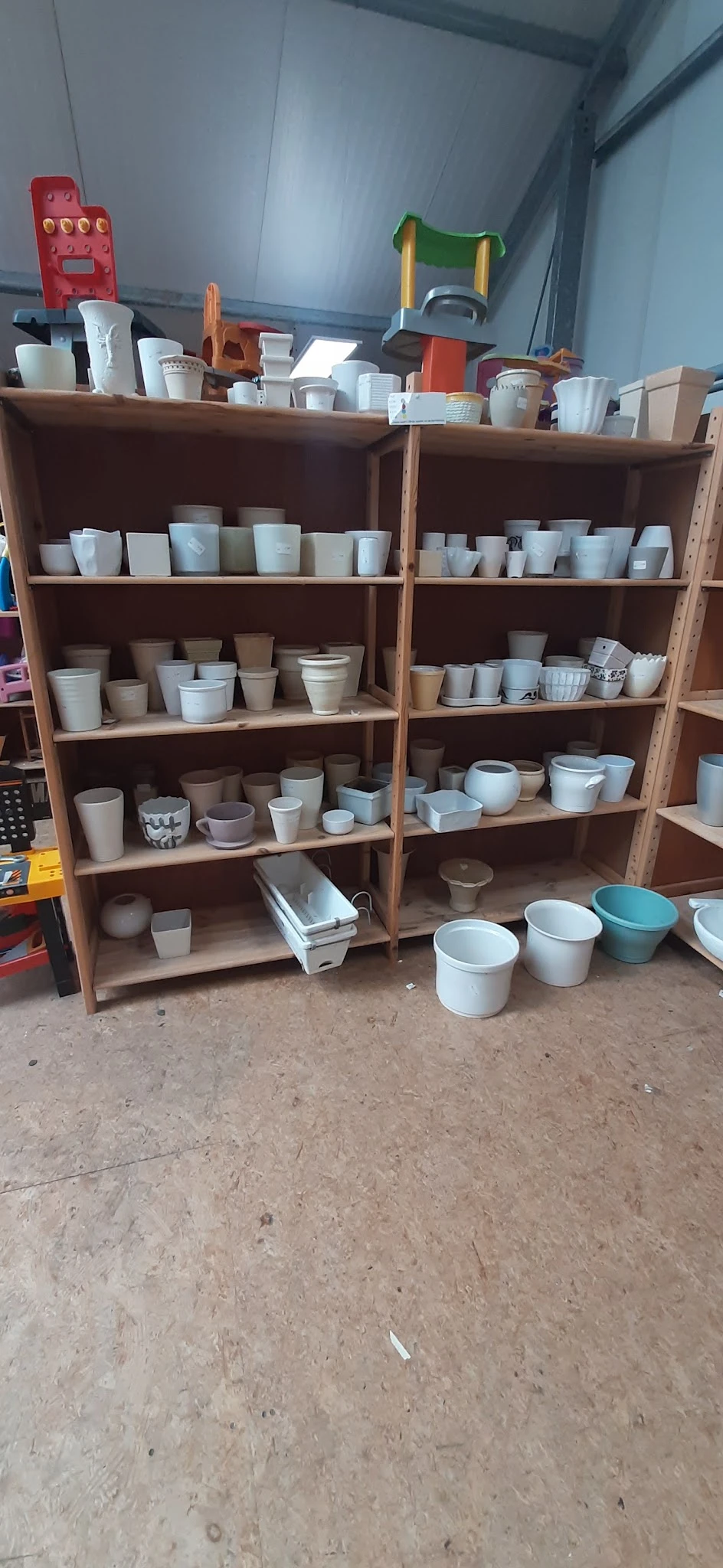 Houten stellingen vol met witte en beige aardewerk, potten en servies in verschillende maten