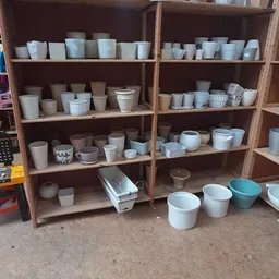 Houten stellingen vol met witte en beige aardewerk, potten en servies in verschillende maten