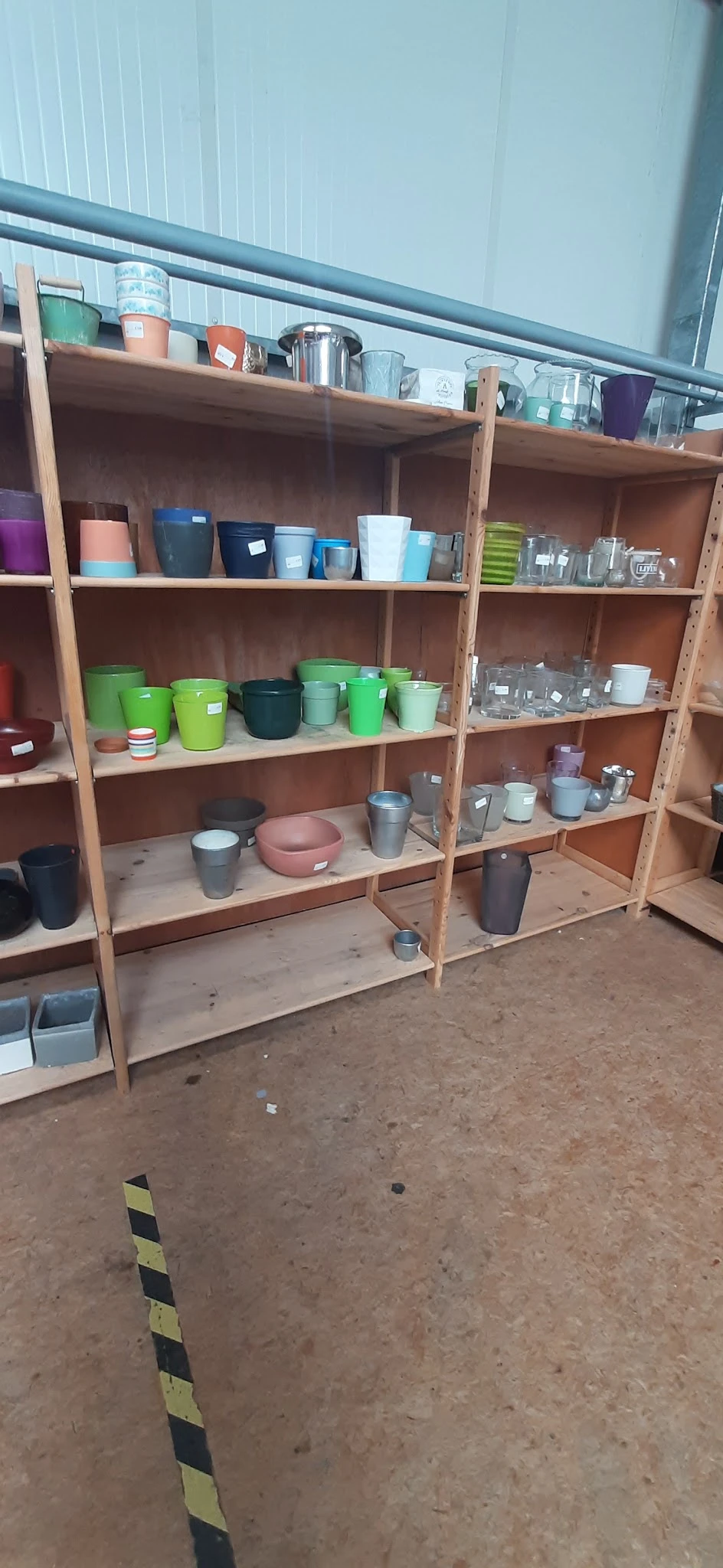 Houten stellingen met diverse huishoudelijke artikelen: gekleurde bekers, pannen, glazen en opslagcontainers