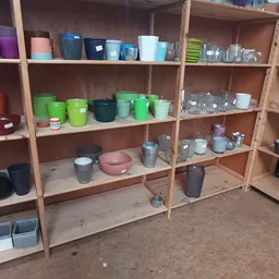 Houten stellingen met diverse huishoudelijke artikelen: gekleurde bekers, pannen, glazen en opslagcontainers