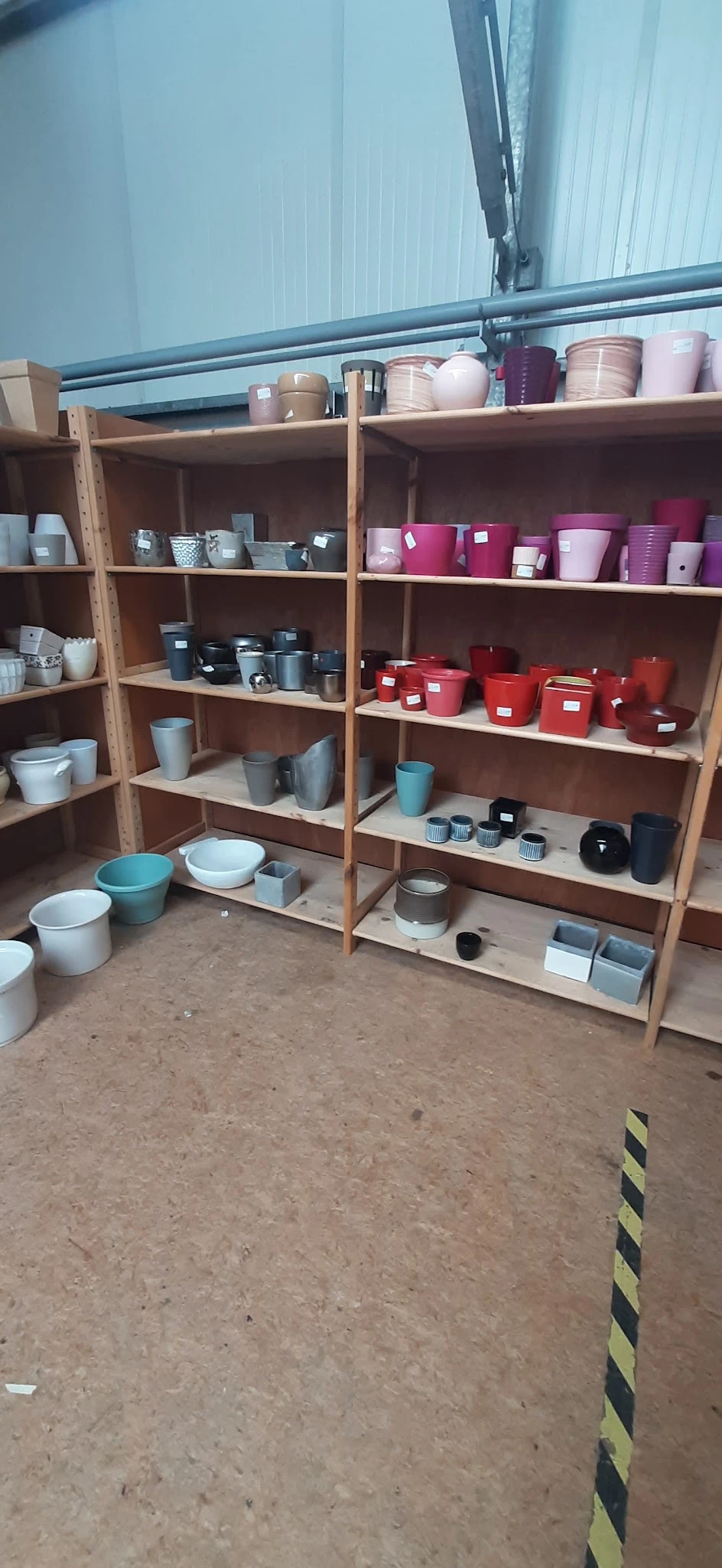 Houten stellingen met uitgestalde huishoudartikelen: kleurrijke potten, bakjes en containers in diverse kleuren