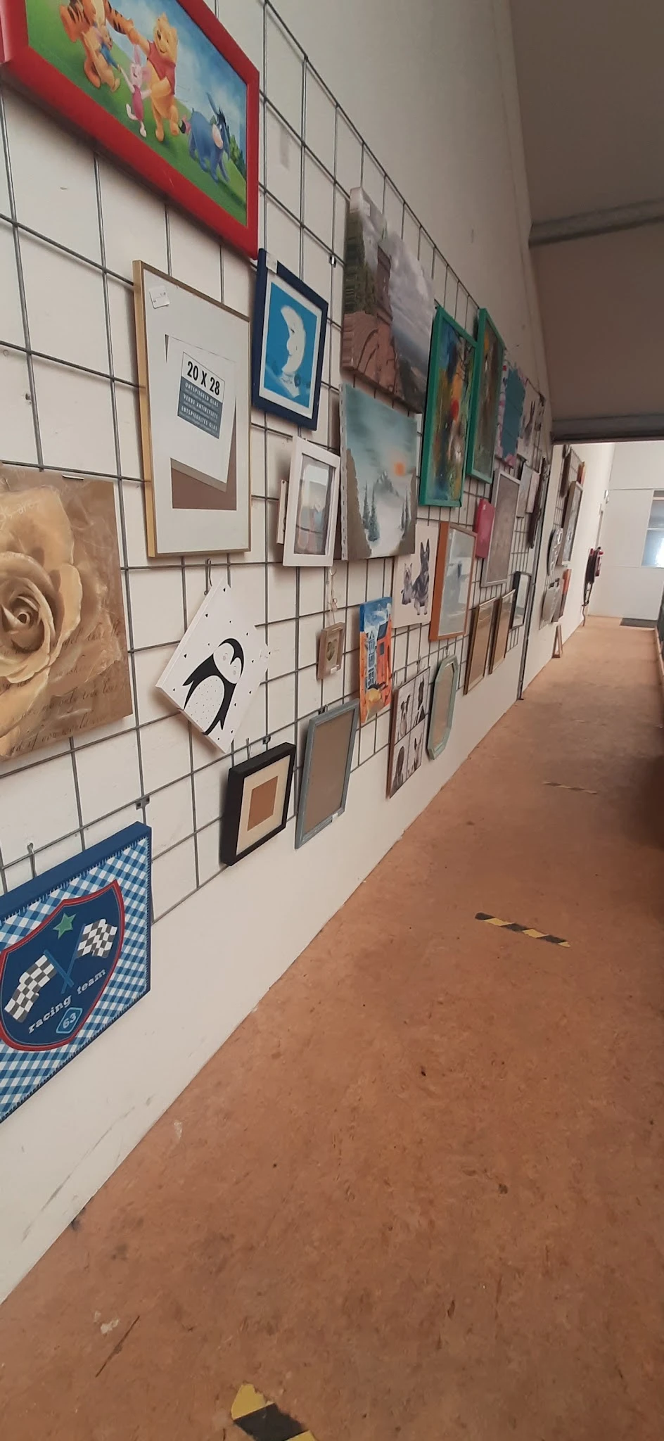 Galerij met kunstwerken en afbeeldingen aan metallisch raster in kringloopwinkel