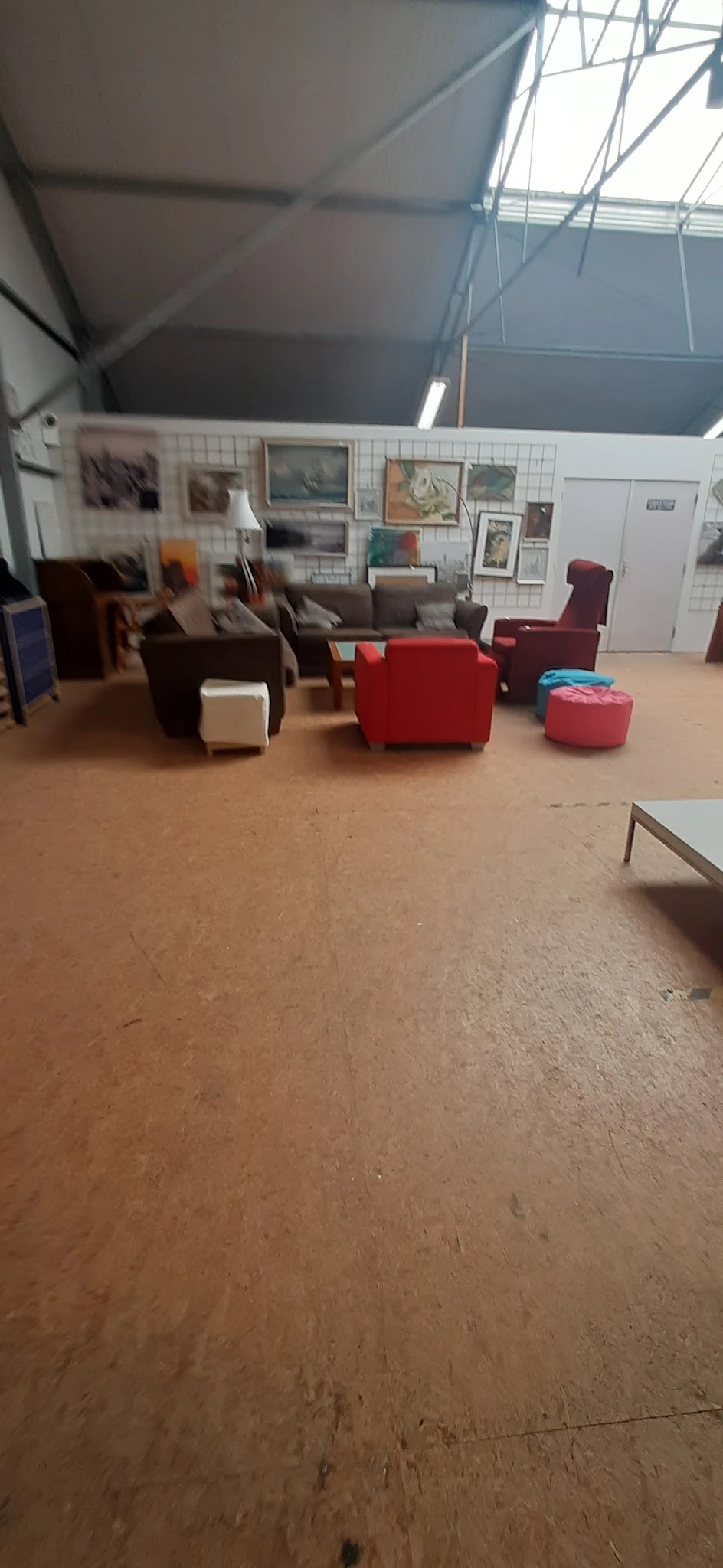 Winkelvloer met diverse meubels: bruine stoelen, rode pouf en fauteuil, stellingen op achtergrond
