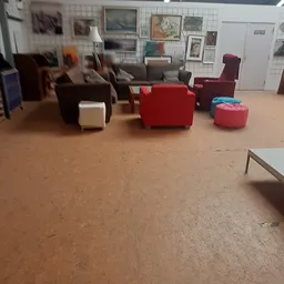 Winkelvloer met diverse meubels: bruine stoelen, rode pouf en fauteuil, stellingen op achtergrond