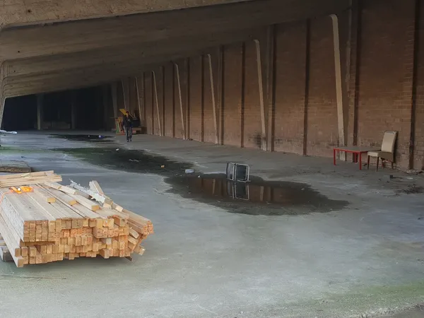 Ruime lege betonnen hal onder constructie met houten steunbalken, gestapeld hout en bouwmateriaal