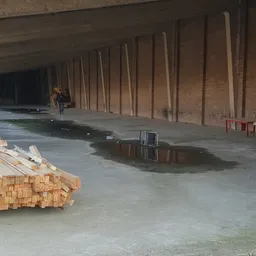 Ruime lege betonnen hal onder constructie met houten steunbalken, gestapeld hout en bouwmateriaal