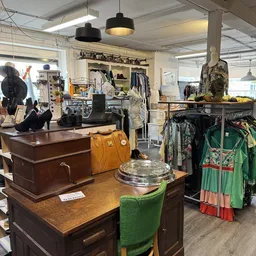 Winkelvloer met diverse meubels, kleding op hangers en spullen uitgestald in een kringloopwinkel