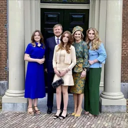 Vijf personen in formele kleding poseren voor een deur met zuilen