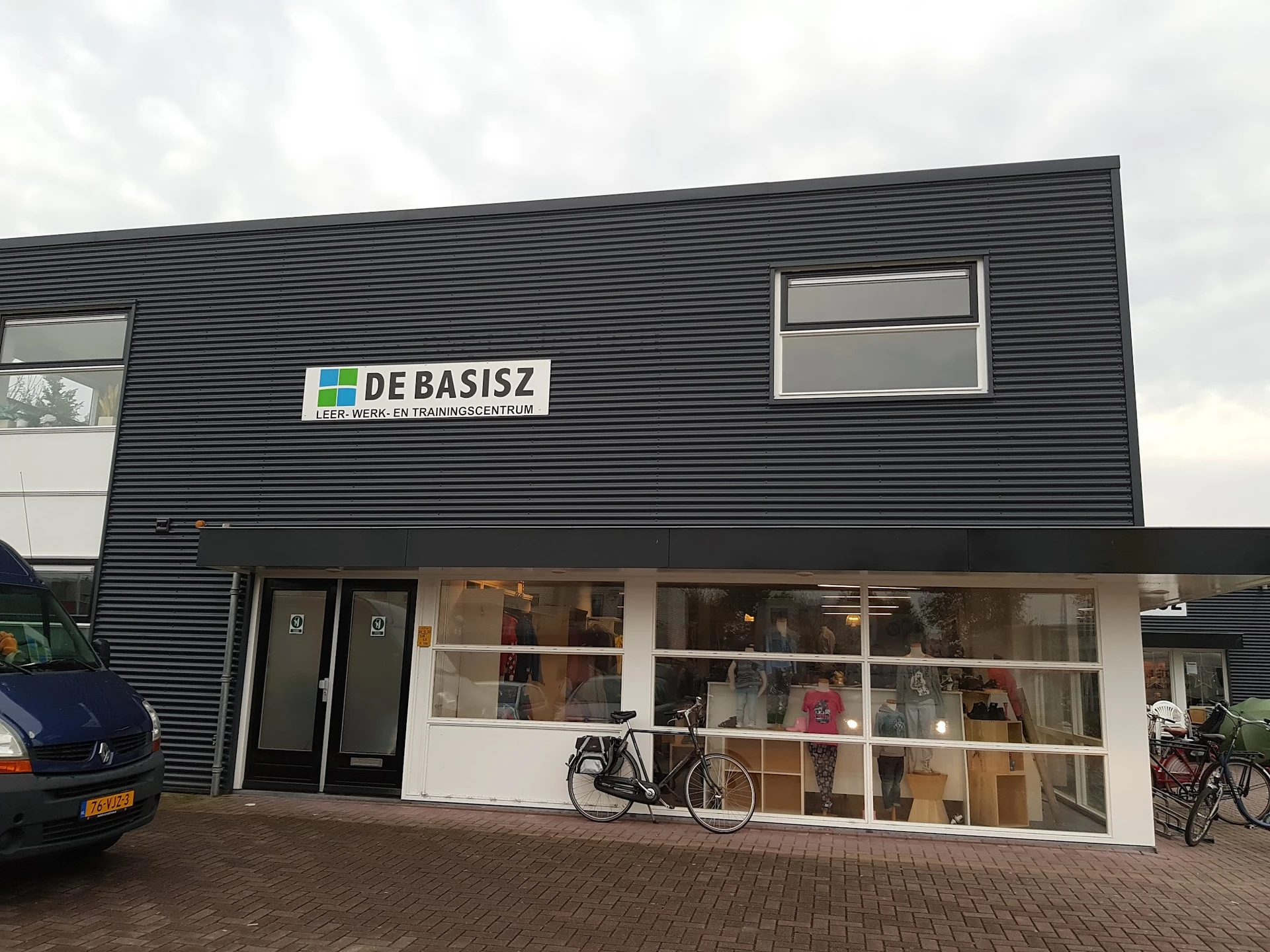 Gevel van kringloopwinkel met zwarte golfplaten, grote ramen en duidelijk zichtbaar logo DE BASISZ