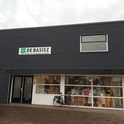 Gevel van kringloopwinkel met zwarte golfplaten, grote ramen en duidelijk zichtbaar logo DE BASISZ