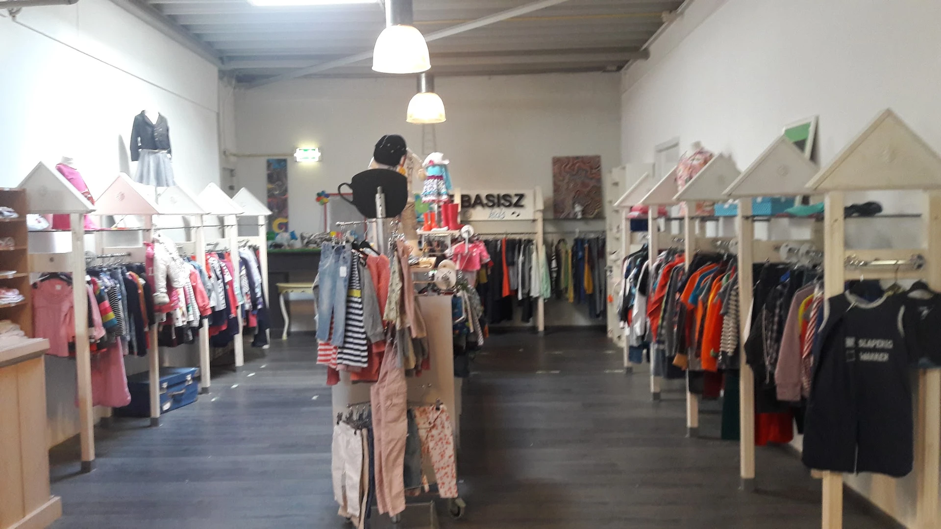 Winkelvloer met rekken vol tweedehands kleding, hangende lampen en een mannequin in het centrum