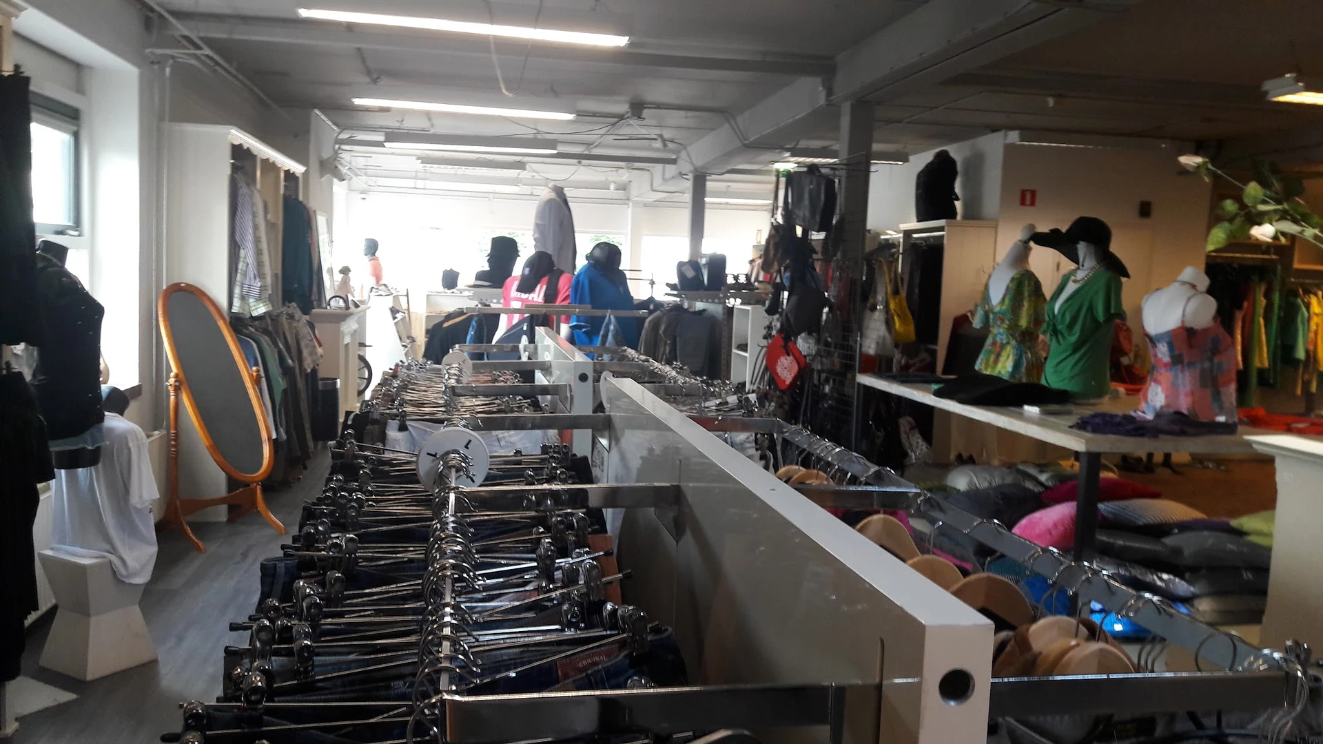 Kringloopwinkelinterieur met rekken tweedehands kleding, klanten in het achtergrond, fluorescente verlichting