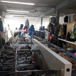 Kringloopwinkelinterieur met rekken tweedehands kleding, klanten in het achtergrond, fluorescente verlichting