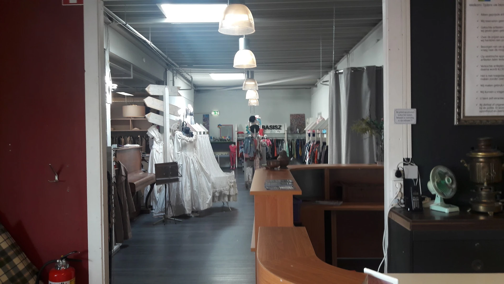 Binnenaanzicht van kringloopwinkel met kledingrekken, hangende kleding, houten toonbank en verlichtingselementen