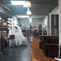Binnenaanzicht van kringloopwinkel met kledingrekken, hangende kleding, houten toonbank en verlichtingselementen
