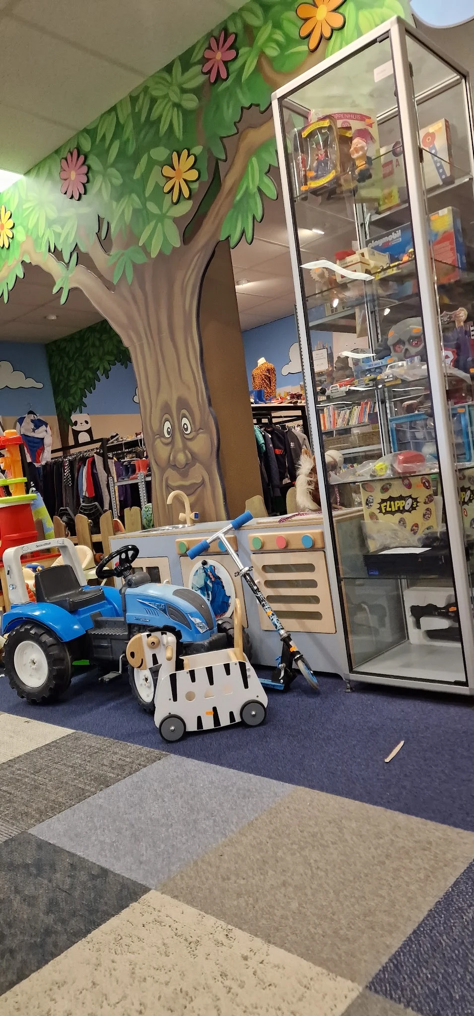 Kindervoertuigen en speelgoed in een kringloopwinkel, waaronder een blauwe driewieler en kinderspeelgoed