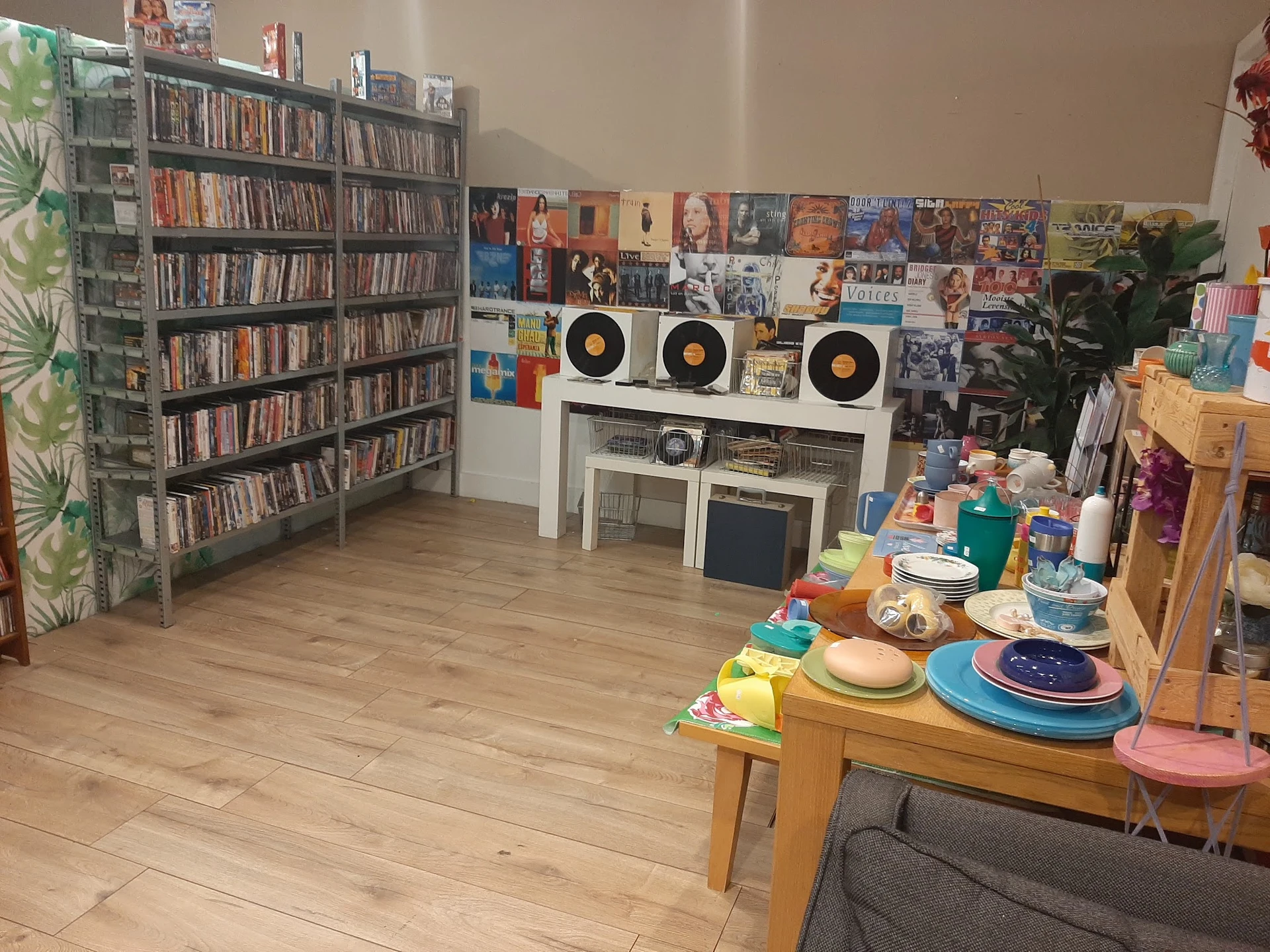 Winkelvloer met cd-kasten, een witte kast met draaitafels, dvd-collectie aan muur, en tafel met serviesgoed en speelgoed