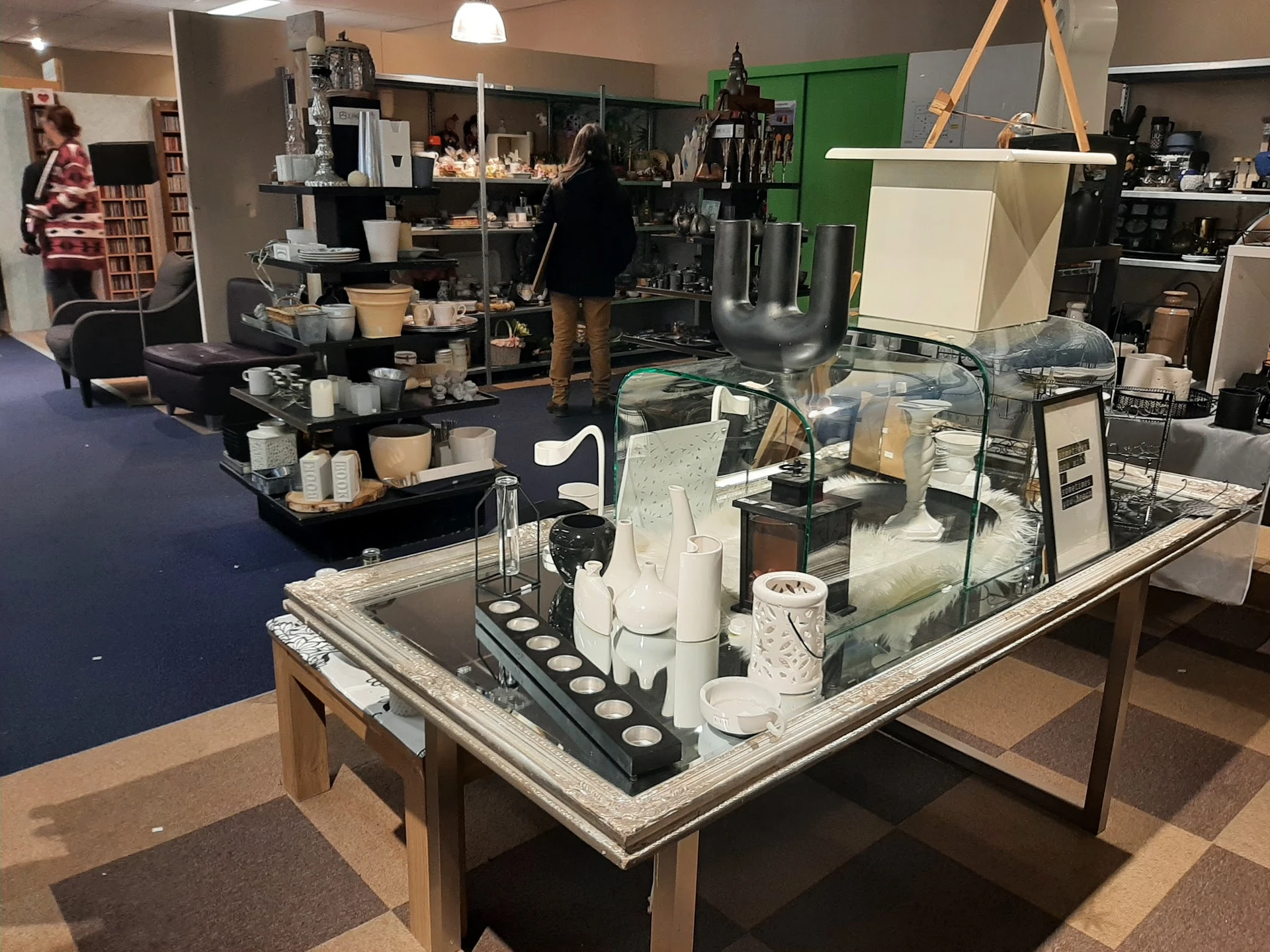 Overzicht van de winkelvloer met toonbanken, schappen en diverse tweedehands artikelen in de kringloopwinkel
