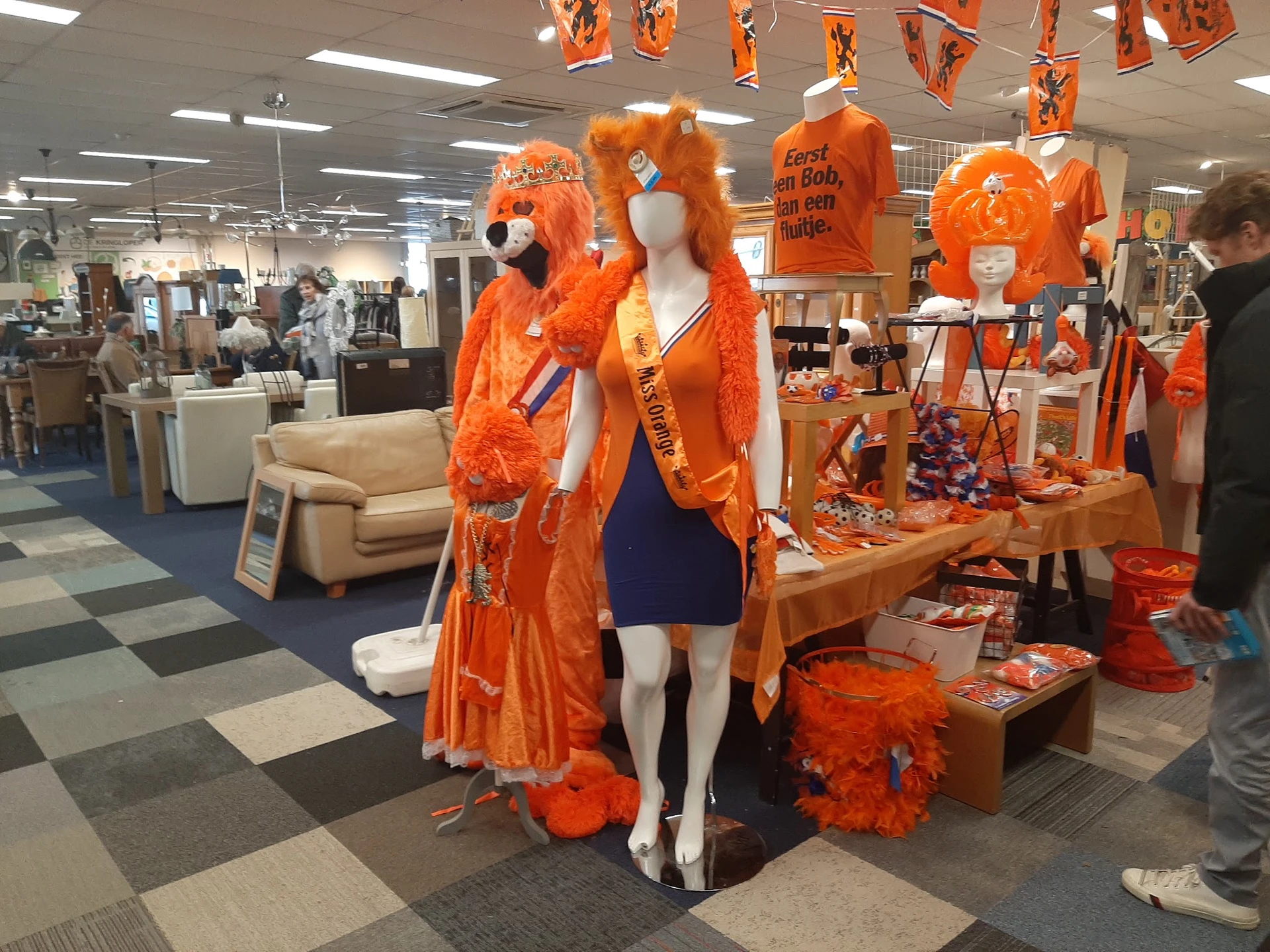 Uitgestalde oranje kleding en accessoires op etalagepoppen en tafels in de winkel
