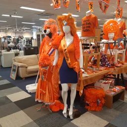 Uitgestalde oranje kleding en accessoires op etalagepoppen en tafels in de winkel