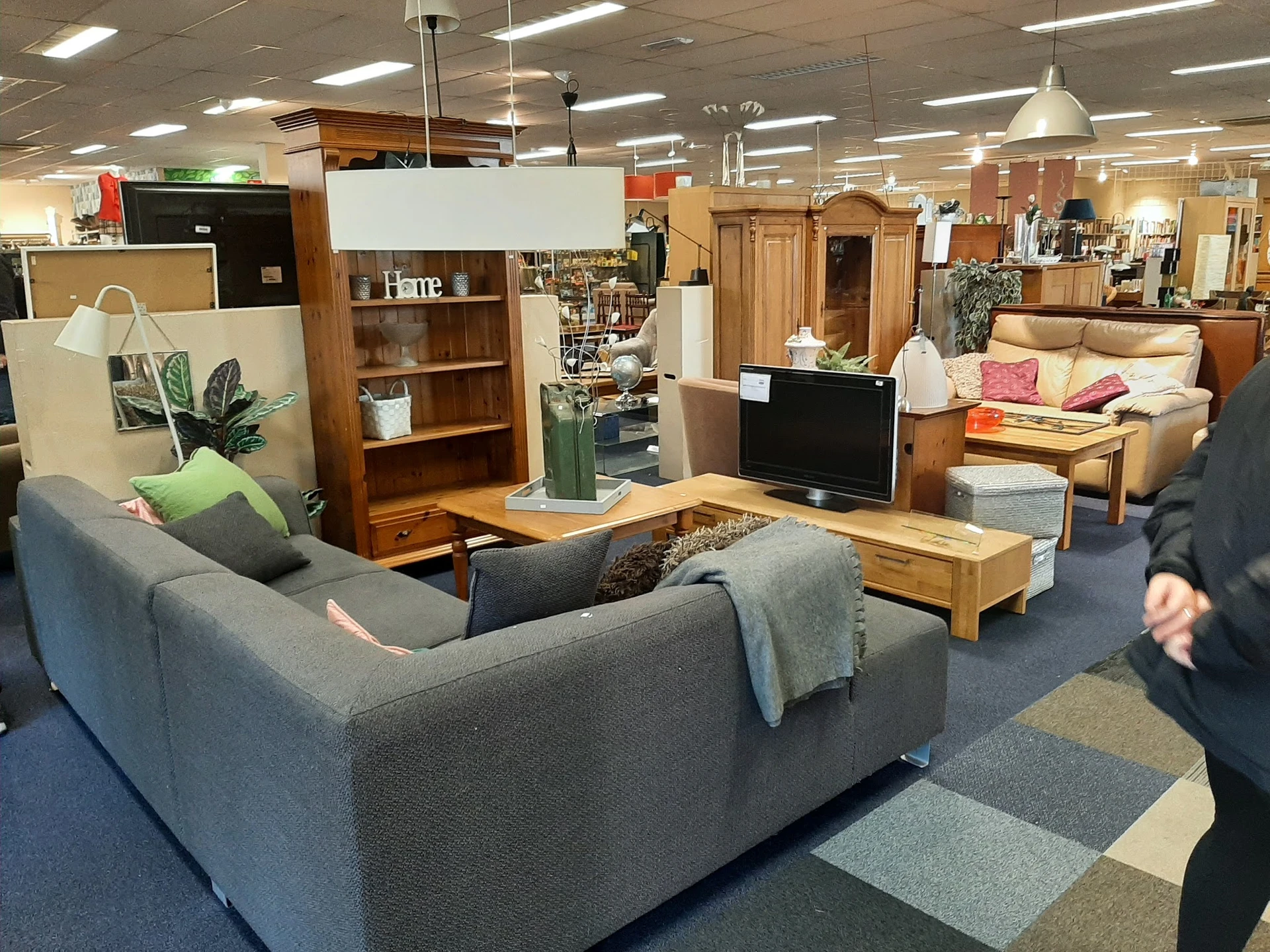 Winkelvloer met meubels: grijze bank, houten kasten, tv-meubel en verscheidene stoelen en tafels