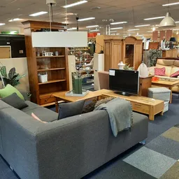 Winkelvloer met meubels: grijze bank, houten kasten, tv-meubel en verscheidene stoelen en tafels
